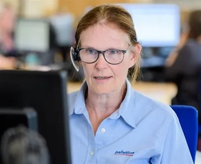A Palletline team member wearing a headset and branded shirt sits at a desk, engaged with a computer in a call centre setting.